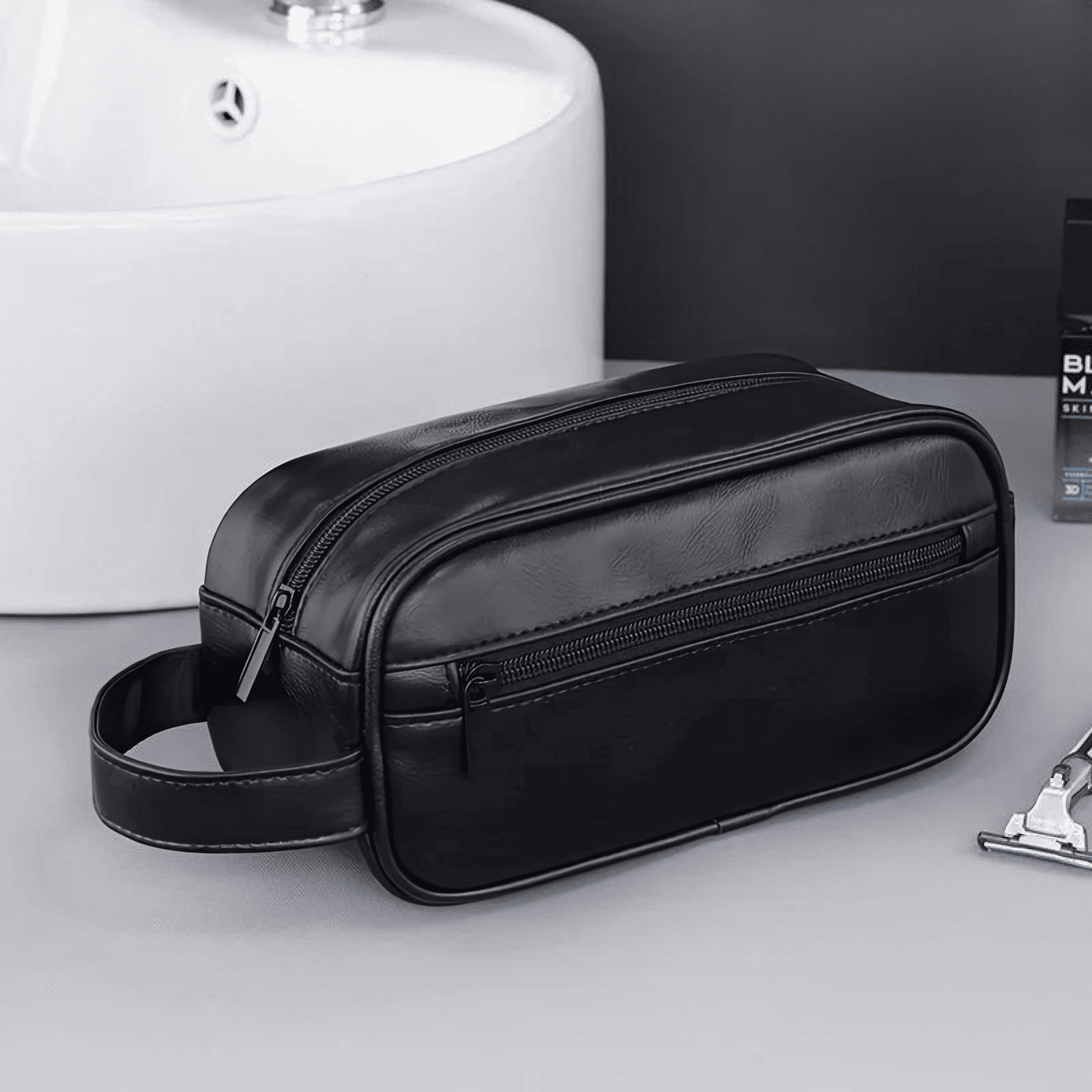 Trousse de toilette homme noire en simili cuir posée près d’un lavabo, idéale pour un usage quotidien ou en déplacement.