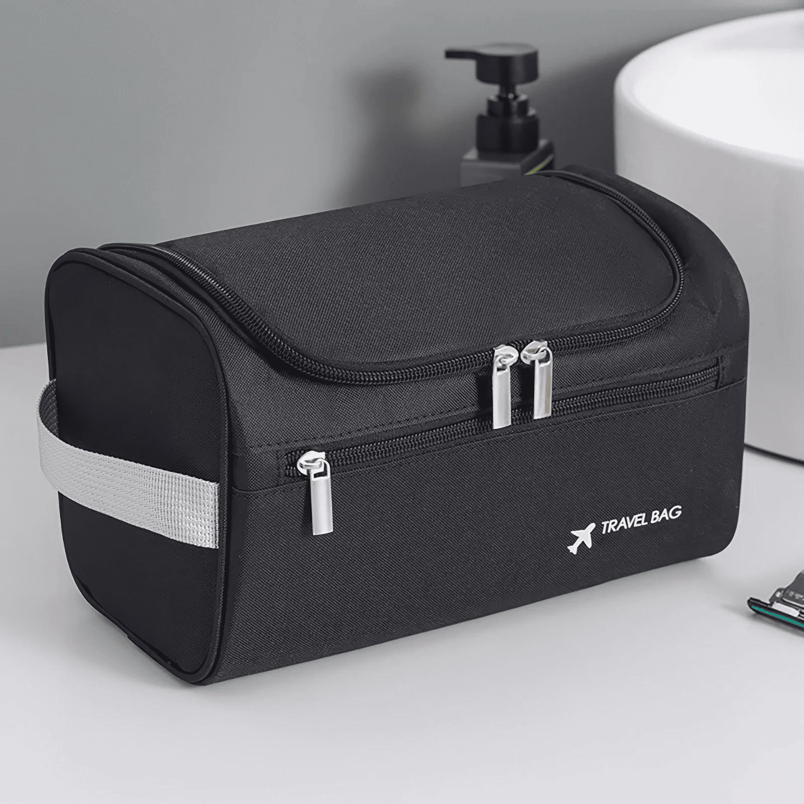 Trousse de toilette voyage avion noire avec poignée latérale, posée dans une salle de bain moderne