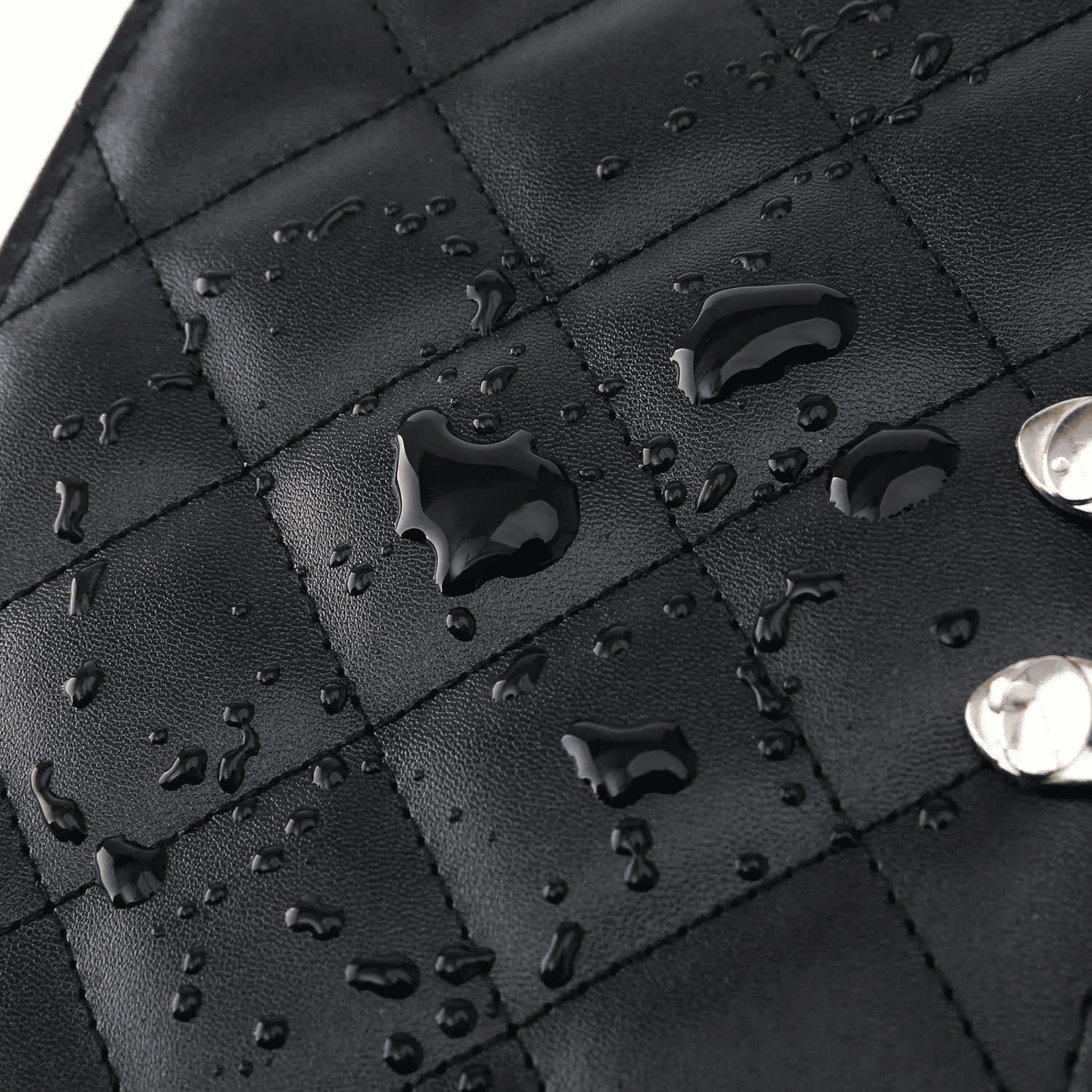 Gros plan sur une grande trousse de toilette femme en simili cuir noir imperméable avec surpiqûres élégantes et perles d’eau en surface.